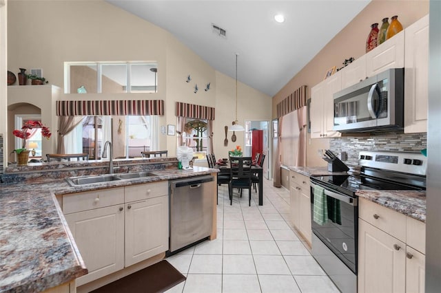 kitchen featuring high vaulted ceiling, decorative light fixtures, appliances with stainless steel finishes, backsplash, and sink