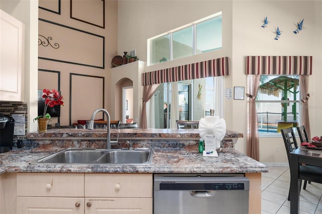 kitchen featuring a towering ceiling, light stone counters, sink, light tile floors, and stainless steel dishwasher