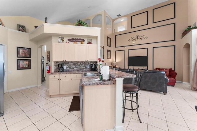 kitchen with high vaulted ceiling, backsplash, a kitchen breakfast bar, sink, and light tile floors