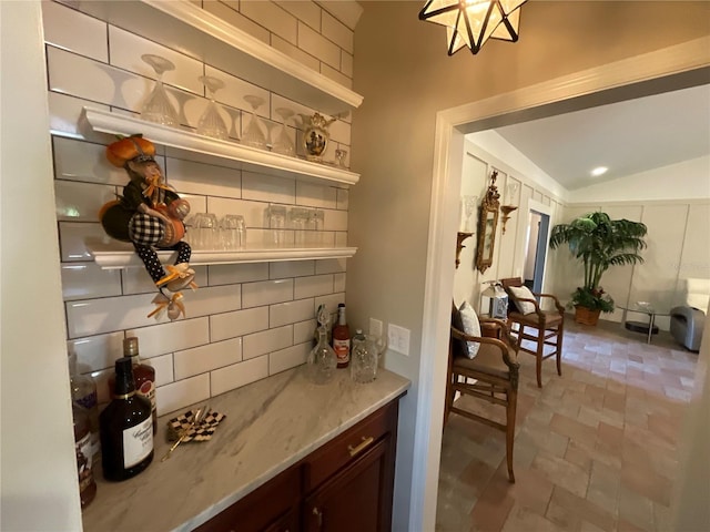 bar with dark brown cabinetry, light stone counters, tasteful backsplash, and light tile floors