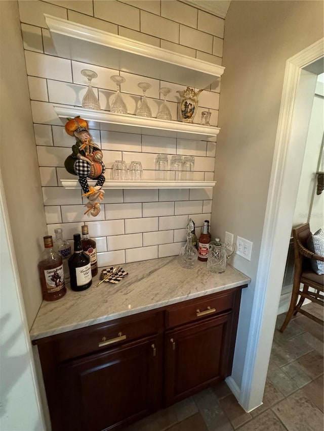 bar featuring dark brown cabinets, tasteful backsplash, dark tile floors, and light stone counters