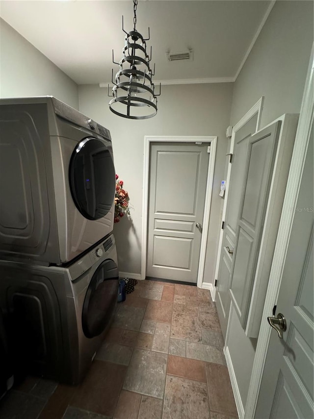 washroom with stacked washer and clothes dryer, ornamental molding, dark tile flooring, and a chandelier