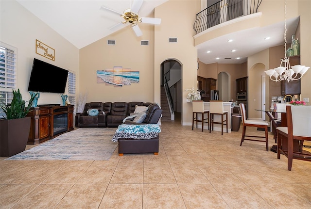 tiled living room with ceiling fan with notable chandelier and high vaulted ceiling