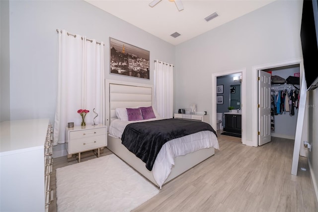 bedroom with a closet, ensuite bathroom, light hardwood / wood-style flooring, ceiling fan, and a walk in closet