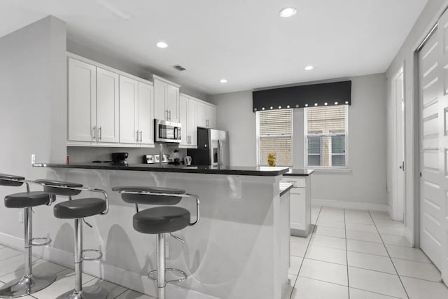 kitchen with white cabinetry, kitchen peninsula, stainless steel appliances, a kitchen bar, and light tile floors