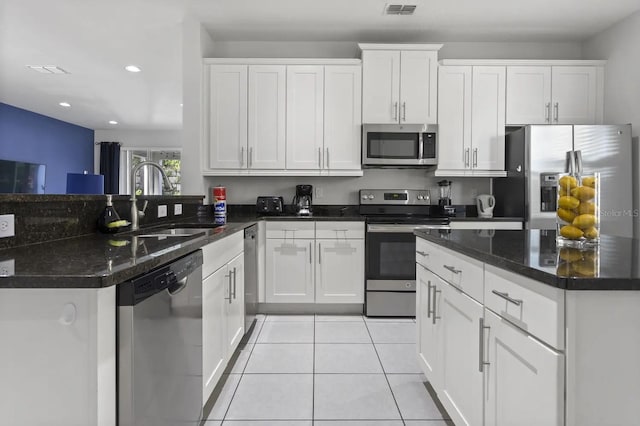 kitchen with appliances with stainless steel finishes, dark stone counters, white cabinetry, sink, and light tile floors