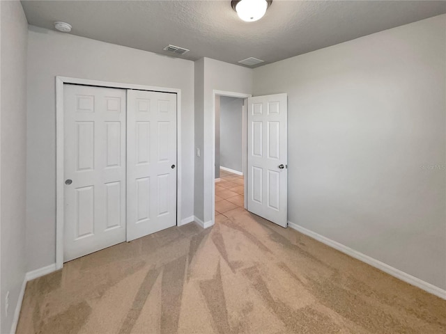 unfurnished bedroom featuring light colored carpet, a textured ceiling, and a closet