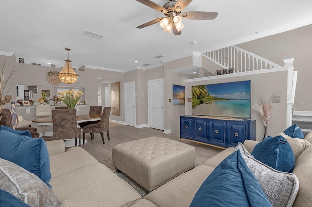 living room with wood-type flooring, ceiling fan with notable chandelier, and ornamental molding