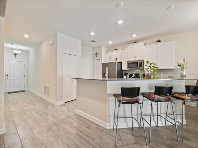 kitchen with a kitchen breakfast bar, light hardwood / wood-style flooring, backsplash, stainless steel appliances, and white cabinetry