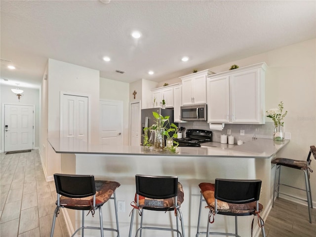 kitchen featuring a breakfast bar area, backsplash, stainless steel appliances, and white cabinets