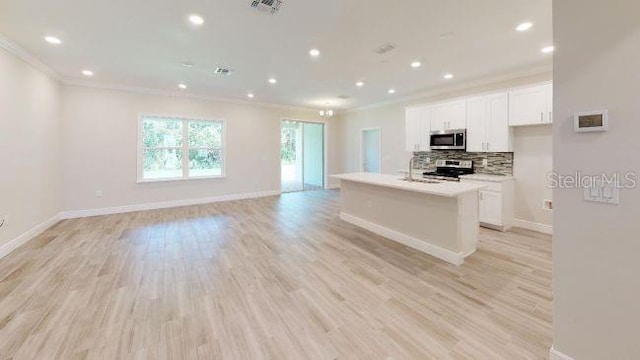 kitchen with an island with sink, white cabinetry, backsplash, ornamental molding, and stainless steel appliances