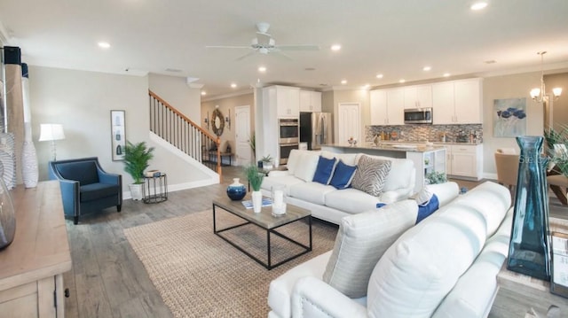 living room with crown molding, wood-type flooring, and ceiling fan with notable chandelier