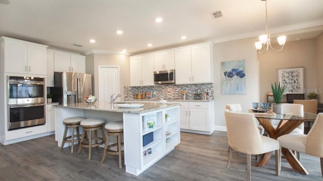 kitchen with pendant lighting, stainless steel appliances, a kitchen island with sink, and white cabinets