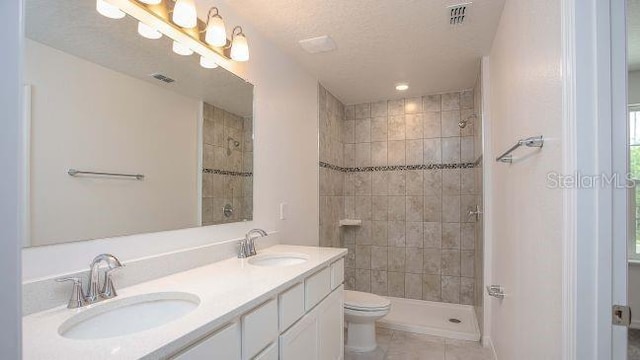 bathroom with tile patterned flooring, tiled shower, vanity, a textured ceiling, and toilet