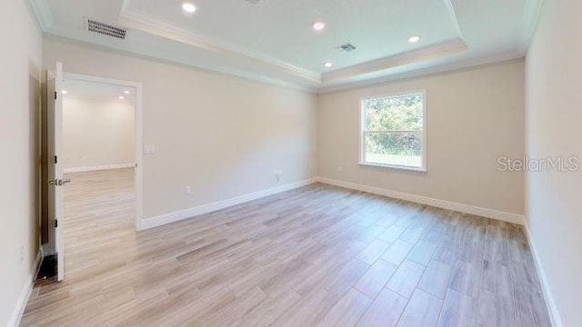 empty room featuring ornamental molding, a tray ceiling, and light hardwood / wood-style floors