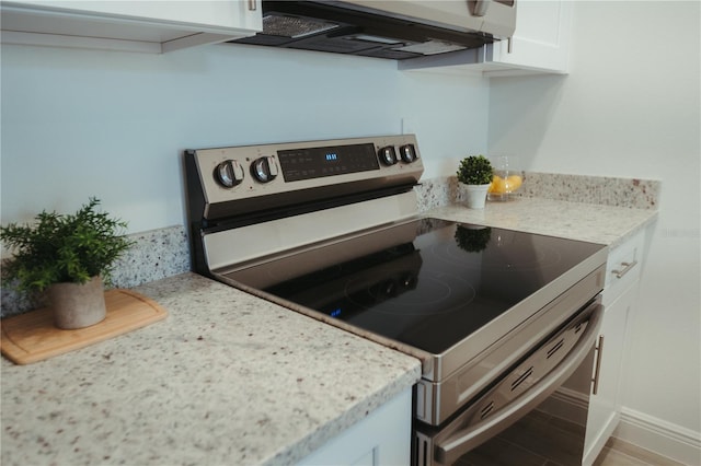 kitchen with white cabinets, stainless steel range with electric stovetop, exhaust hood, and light stone countertops