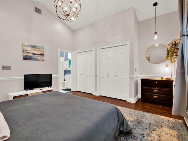 bedroom featuring dark hardwood / wood-style flooring, high vaulted ceiling, ensuite bathroom, a chandelier, and two closets