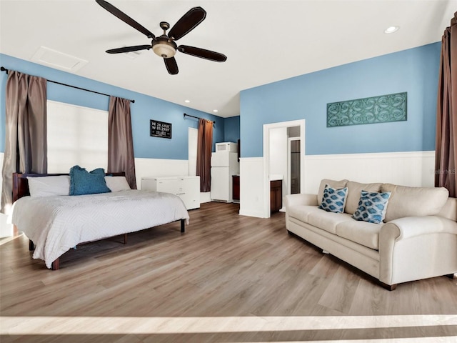 bedroom with ceiling fan, white refrigerator, light wood-type flooring, and ensuite bath