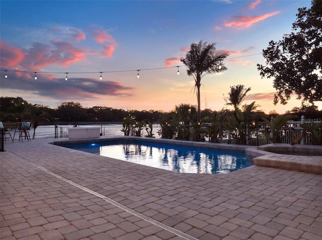 pool at dusk featuring a patio area and a water view