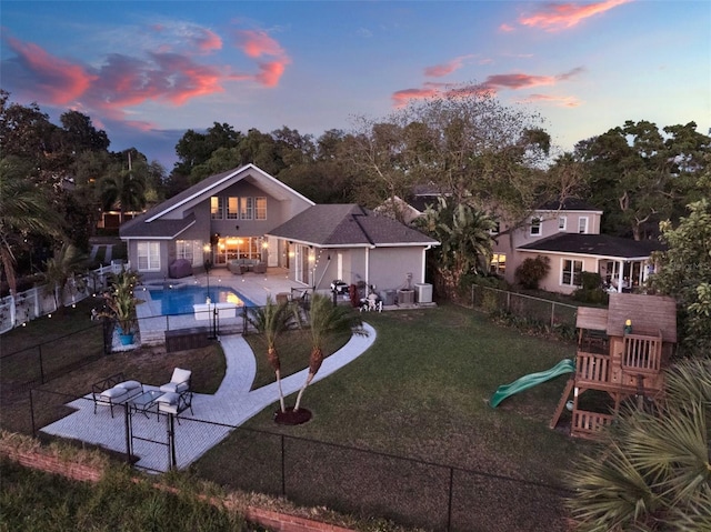 back house at dusk with a lawn, a fenced in pool, an outdoor hangout area, a patio area, and a playground