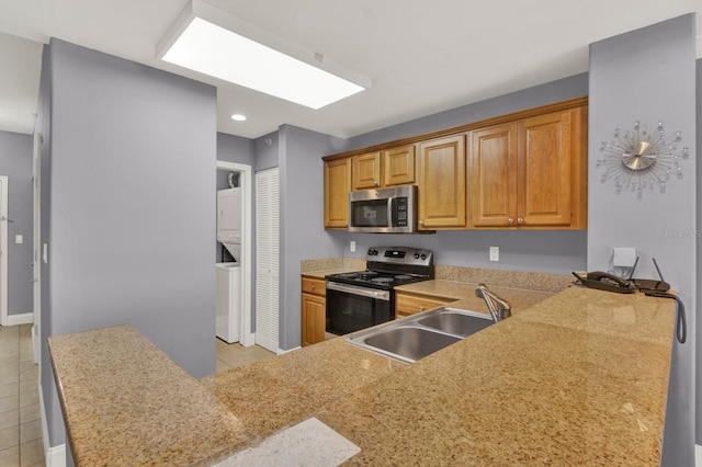 kitchen with sink, light tile patterned floors, stacked washing maching and dryer, appliances with stainless steel finishes, and kitchen peninsula