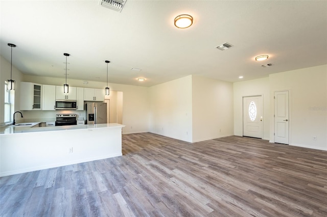 kitchen with pendant lighting, wood-type flooring, sink, white cabinets, and appliances with stainless steel finishes