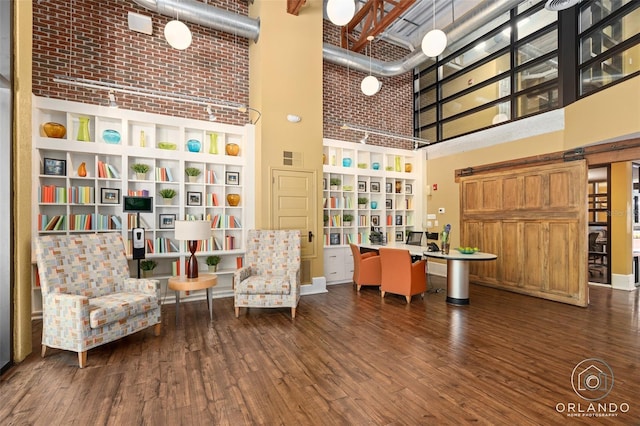 sitting room with a barn door, brick wall, a high ceiling, and dark hardwood / wood-style floors