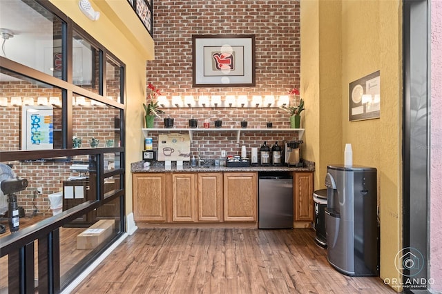 bar with refrigerator, brick wall, wood-type flooring, and dark stone counters