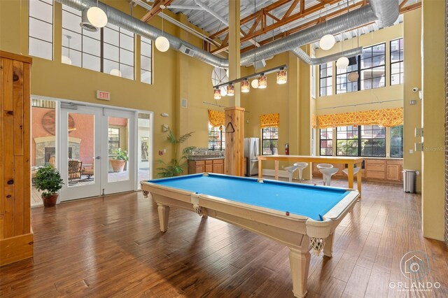 game room with a healthy amount of sunlight, wood-type flooring, and a towering ceiling