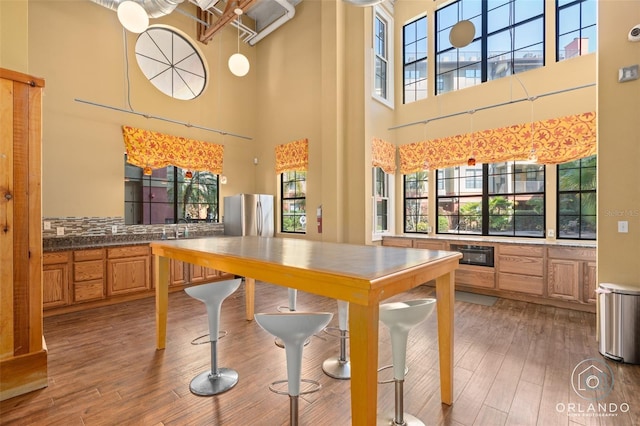 kitchen with sink, stainless steel refrigerator, a high ceiling, and hardwood / wood-style floors