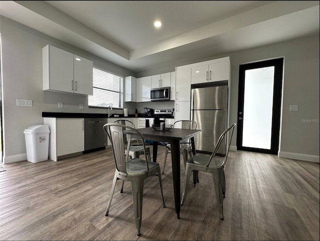 kitchen with sink, white cabinetry, a raised ceiling, hardwood / wood-style floors, and stainless steel appliances