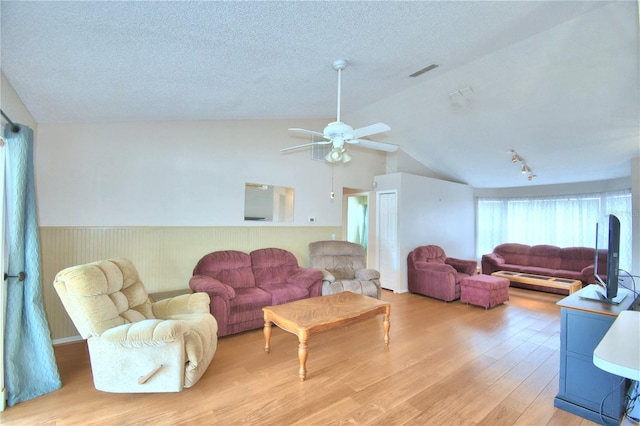 living room with wood walls, vaulted ceiling, ceiling fan, a textured ceiling, and light hardwood / wood-style floors