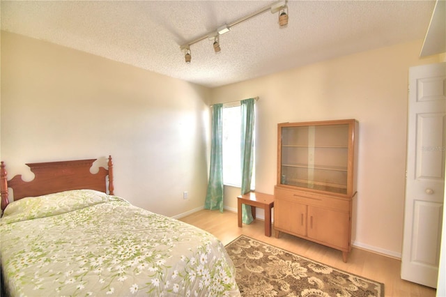 bedroom with light hardwood / wood-style floors, a textured ceiling, and track lighting