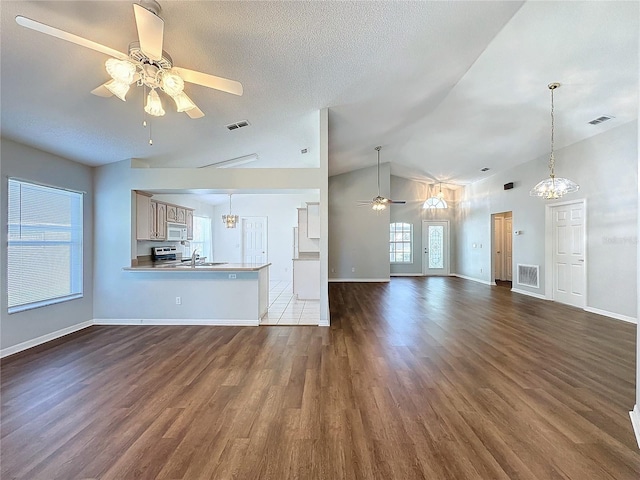 unfurnished living room with a textured ceiling, ceiling fan with notable chandelier, lofted ceiling, and dark wood-type flooring