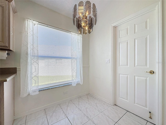 unfurnished dining area featuring plenty of natural light, light tile patterned flooring, a textured ceiling, and an inviting chandelier