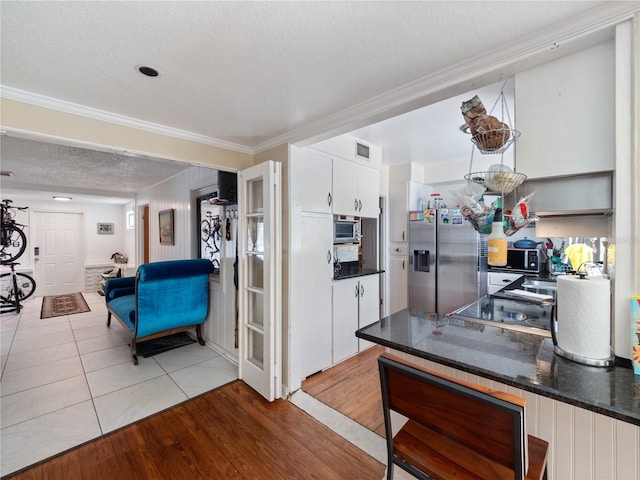 kitchen with crown molding, white cabinets, stainless steel fridge, and light tile floors