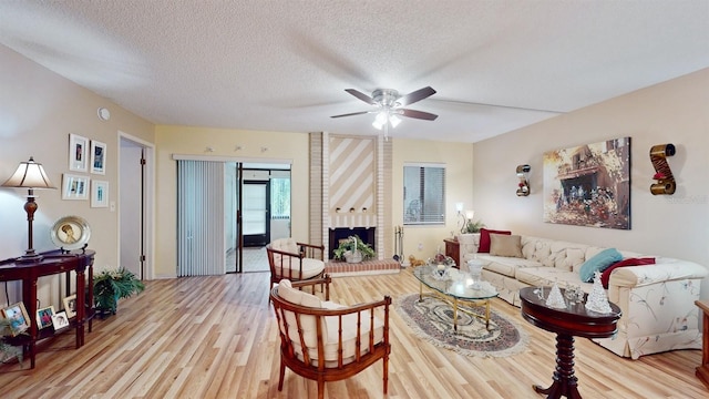 living room featuring a fireplace, ceiling fan, a textured ceiling, and light wood-type flooring