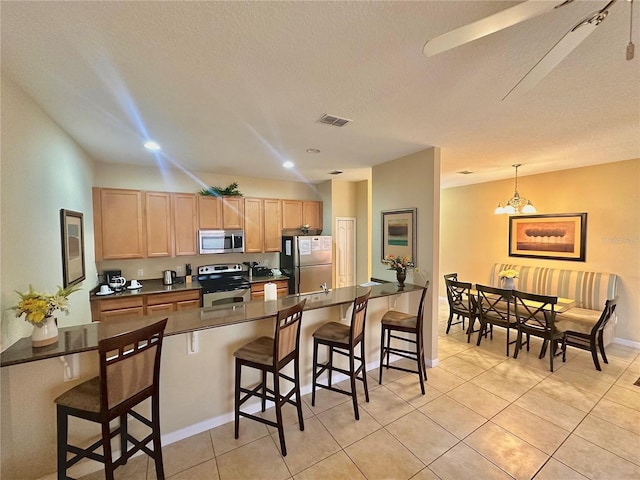 kitchen featuring pendant lighting, light tile patterned floors, a textured ceiling, stainless steel appliances, and a kitchen breakfast bar