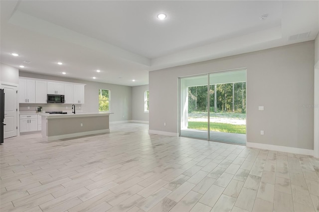 interior space with white cabinets, an island with sink, sink, refrigerator, and light hardwood / wood-style floors