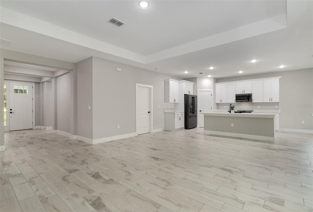 unfurnished living room featuring light wood-type flooring and a tray ceiling