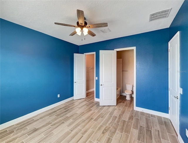 unfurnished bedroom featuring a closet, light wood-type flooring, connected bathroom, a spacious closet, and ceiling fan