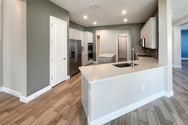 kitchen featuring white cabinets, sink, backsplash, stainless steel appliances, and light hardwood / wood-style flooring