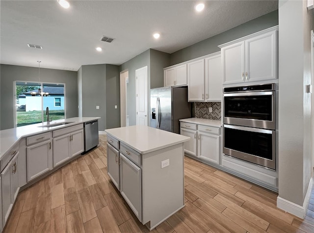 kitchen featuring a kitchen island, stainless steel appliances, tasteful backsplash, white cabinetry, and sink