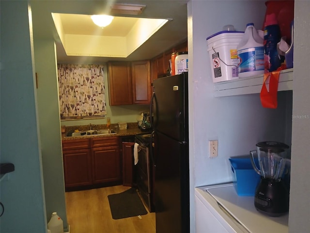 kitchen featuring washer / clothes dryer, black appliances, a tray ceiling, sink, and light hardwood / wood-style floors