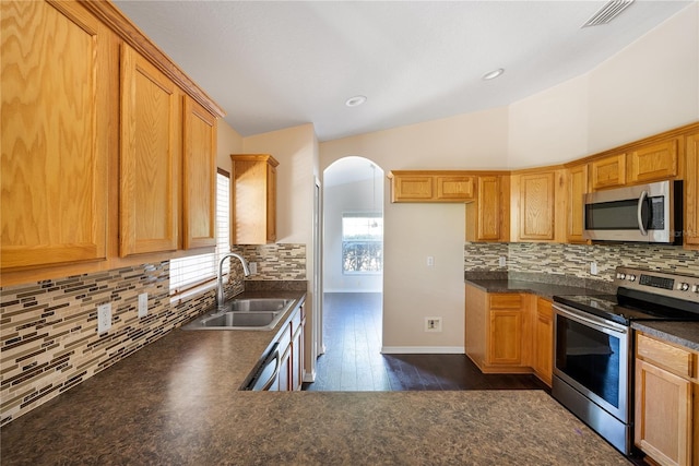 kitchen with appliances with stainless steel finishes, vaulted ceiling, dark hardwood / wood-style floors, tasteful backsplash, and sink