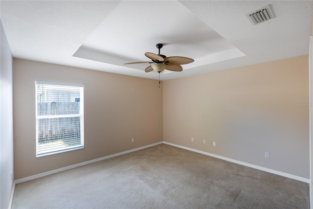 carpeted empty room with a healthy amount of sunlight, a raised ceiling, and ceiling fan