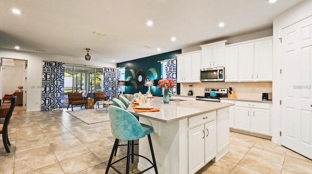 kitchen featuring white cabinets, stainless steel appliances, a kitchen bar, and a kitchen island with sink