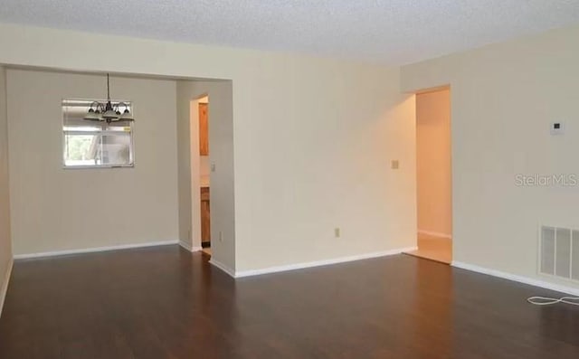 unfurnished room featuring dark wood-type flooring, a notable chandelier, and a textured ceiling