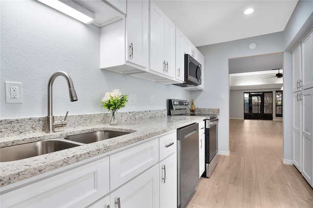 kitchen with stainless steel appliances, white cabinetry, a sink, and light stone countertops