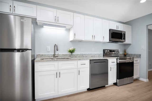 kitchen with white cabinets, light stone countertops, stainless steel appliances, light wood-type flooring, and a sink